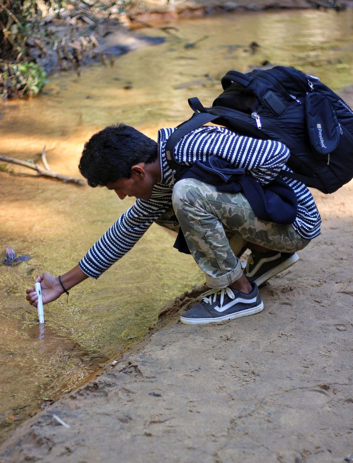 A researcher crouching at the water's edge to draw a sample for field testing